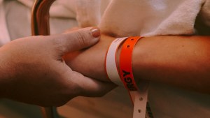 Two people hold hands, one wearing an orange hospital bracelet.